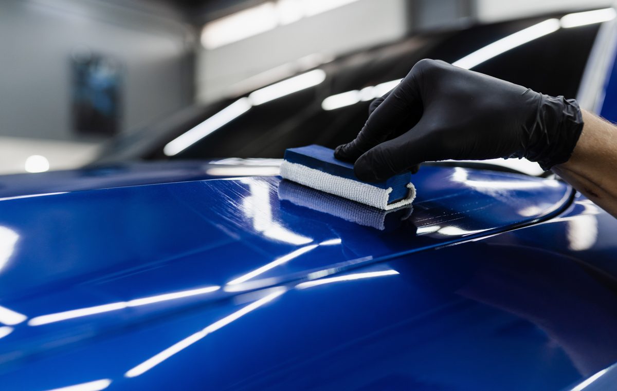 Ceramic coating being hand-applied to a deep blue hood with a mirror-gloss finish
