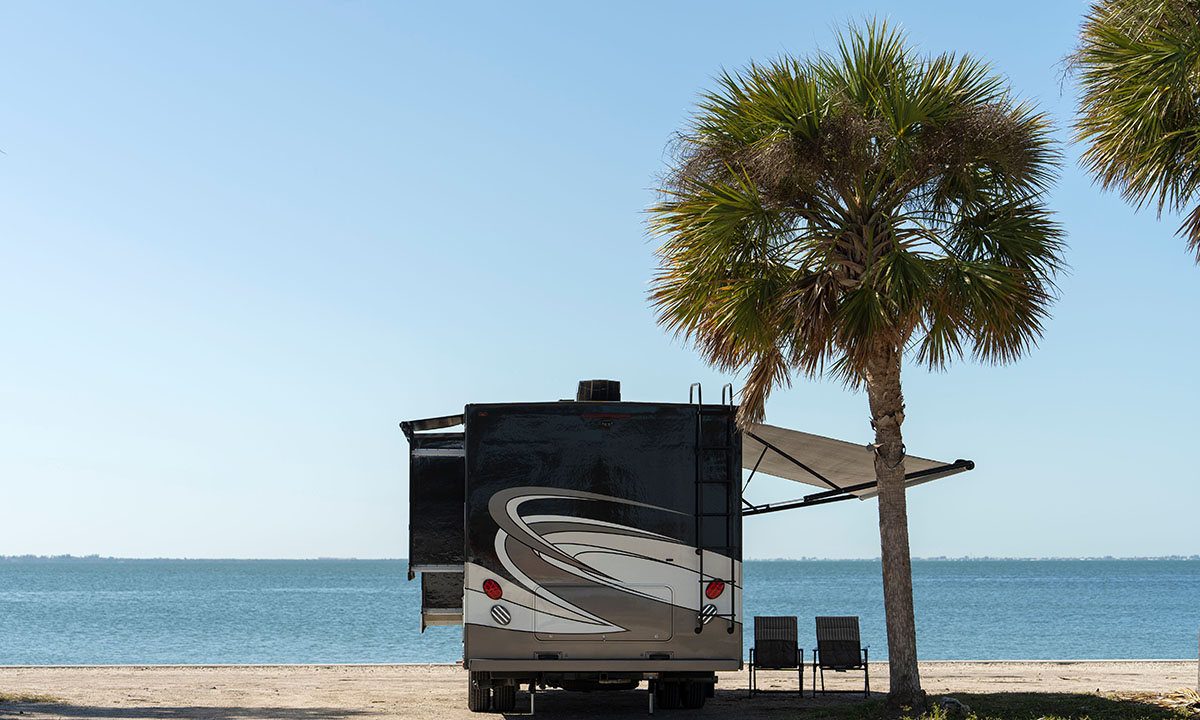 White motorhome parked on a beach beside palm trees